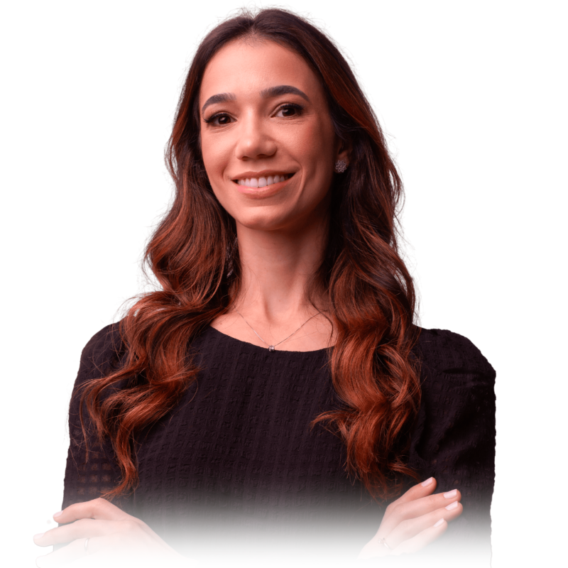 Foto da Dra. Livia. Mulher sorridente de cabelos longos e ondulados, braços cruzados e blusa preta.